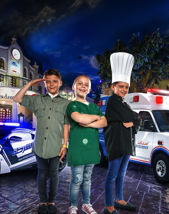 Children in costumes at KidZania Dubai, posing as a police officer, chef, and shopkeeper.