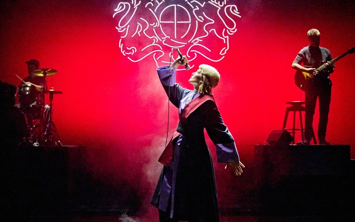 Performer singing on stage during Inter Alia show on Broadway with musicians in the background.