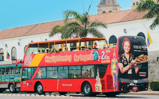 Cartagena hop on hop off tour bus with passengers near historic building.