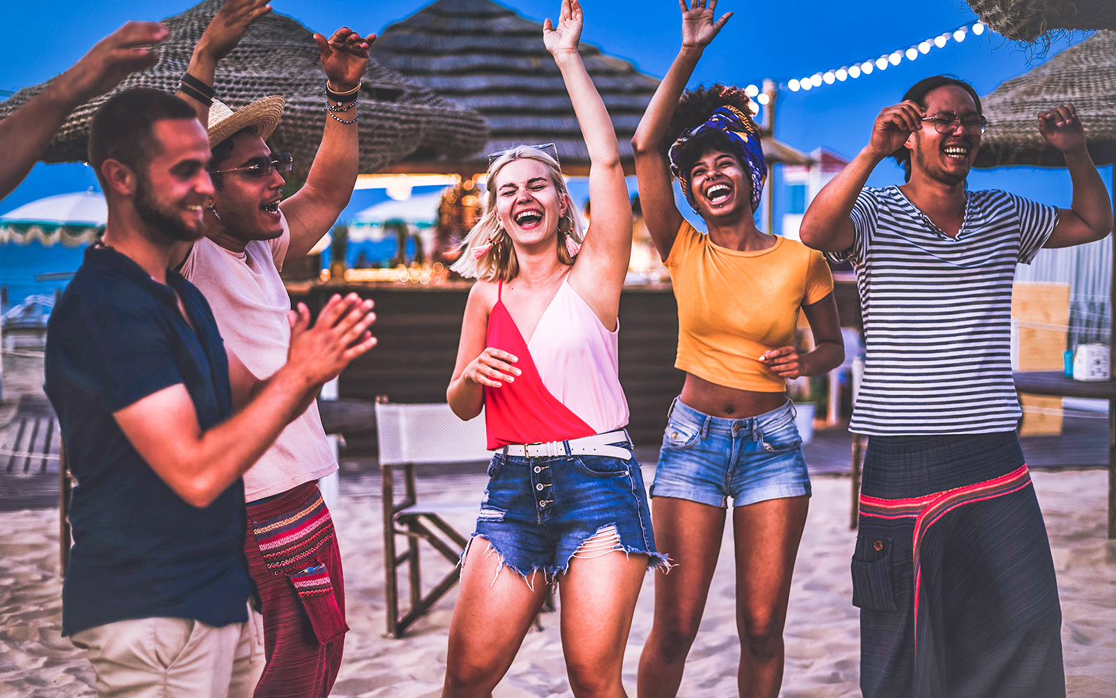 Group of happy multiracial friends dancing at sunrise beach party in summer vacation