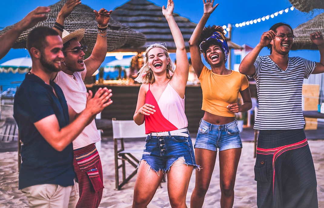 Group of happy multiracial friends dancing at sunrise beach party in summer vacation