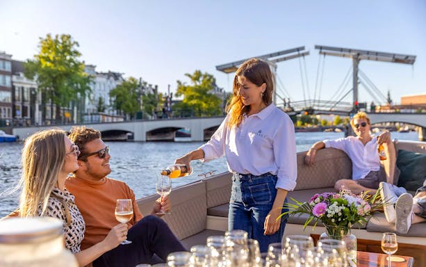 Host serving drinks to guests on a luxury cruise in Amsterdam with a bridge in the background.