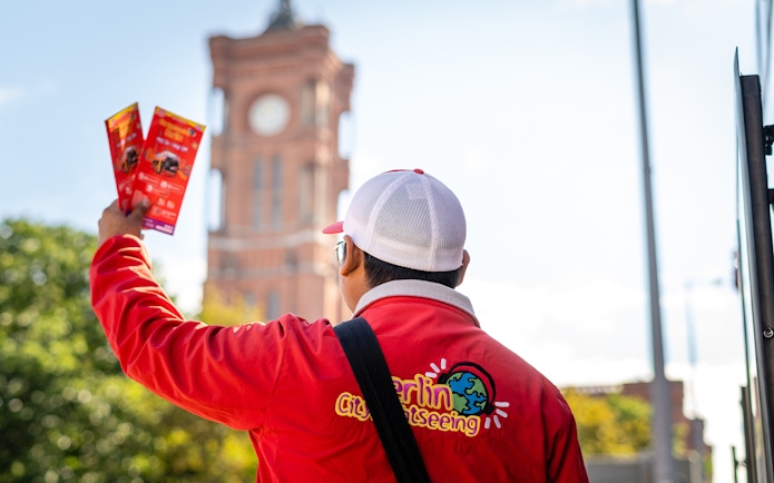 Vendor holding tickets for Berlin Hop On & Hop Off tour near Rotes Rathaus.