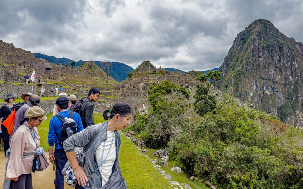 Tourists with guide overlooking Machu Picchu ruins in Peru.