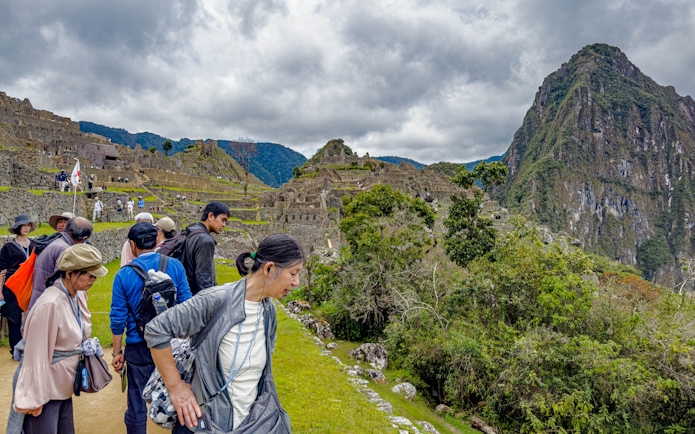 Tourists with guide overlooking Machu Picchu ruins in Peru.
