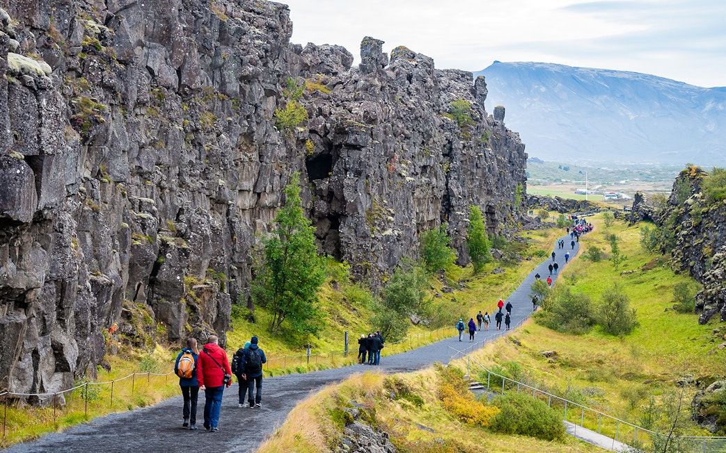Visitors walking along a path between rocky cliffs at Thingvellir National Park on Golden Circle tour.