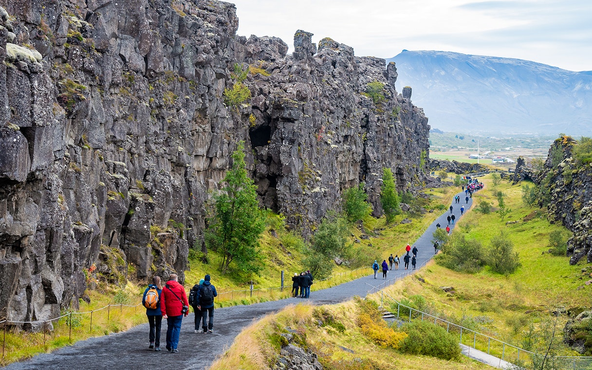 Visitors walking along a path between rocky cliffs at Thingvellir National Park on Golden Circle tour.