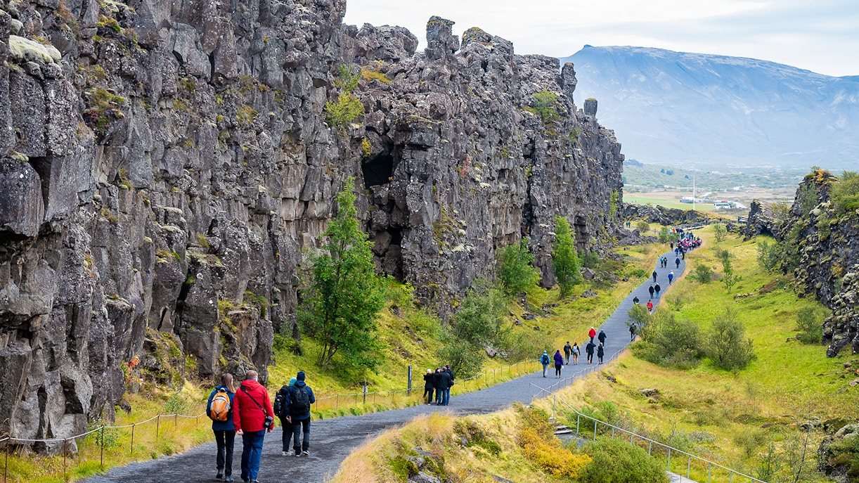 Visitors walking along a path between rocky cliffs at Thingvellir National Park on Golden Circle tour.