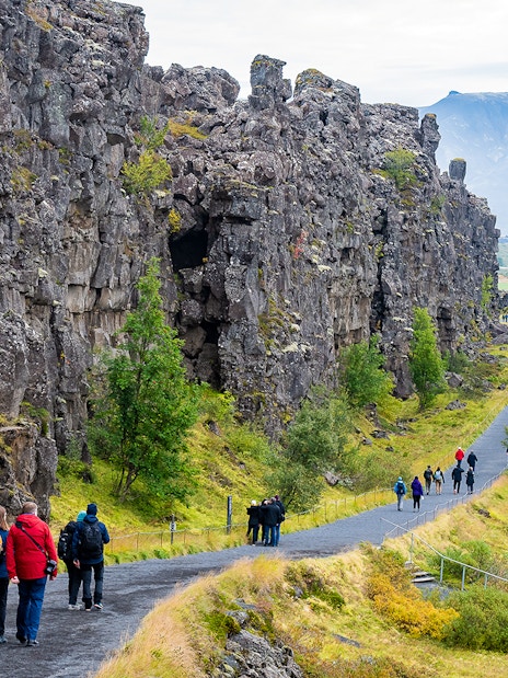 Visitors walking along a path between rocky cliffs at Thingvellir National Park on Golden Circle tour.