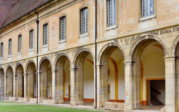 Cluny Abbey exterior with arched stone columns and windows in France.