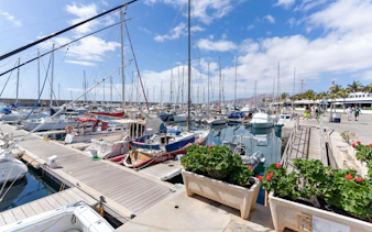 Boats docked at Puerto del Carmen marina with clear skies and waterfront walkway.