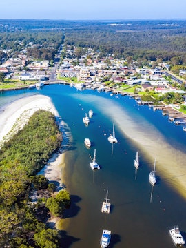 Aerial view of boats and yachts moored in Jervis Bay, surrounded by lush greenery and coastal town.