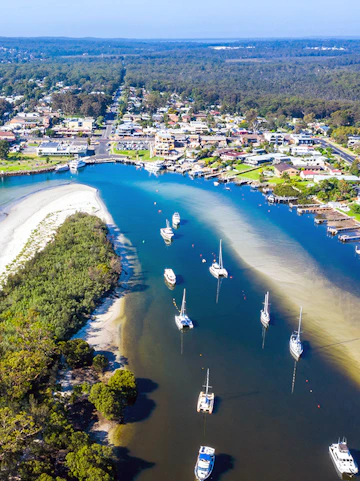 Aerial view of boats and yachts moored in Jervis Bay, surrounded by lush greenery and coastal town.