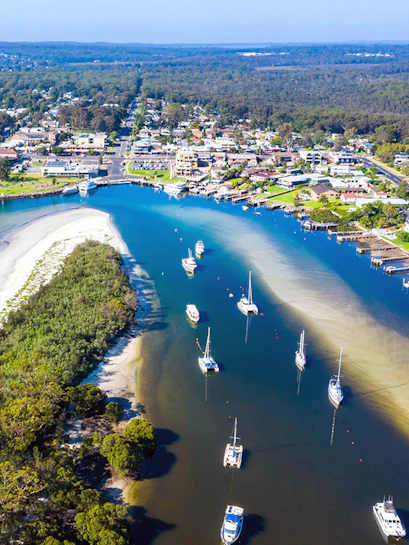 Aerial view of boats and yachts moored in Jervis Bay, surrounded by lush greenery and coastal town.