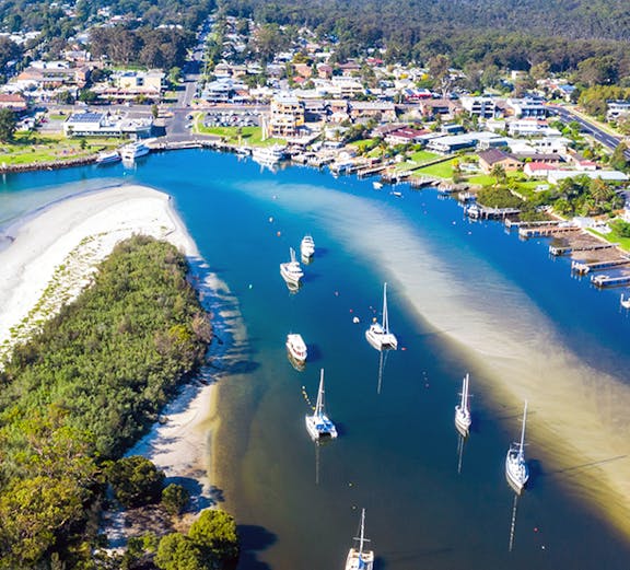 Aerial view of boats and yachts moored in Jervis Bay, surrounded by lush greenery and coastal town.