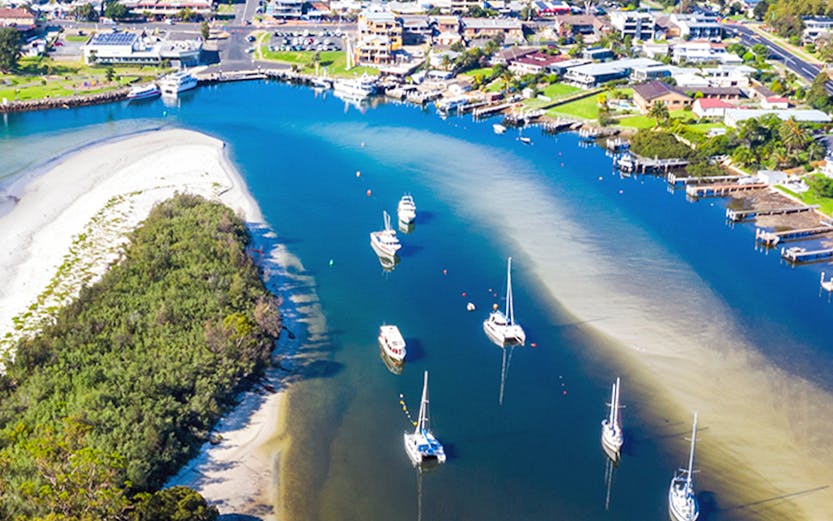 Aerial view of boats and yachts moored in Jervis Bay, surrounded by lush greenery and coastal town.