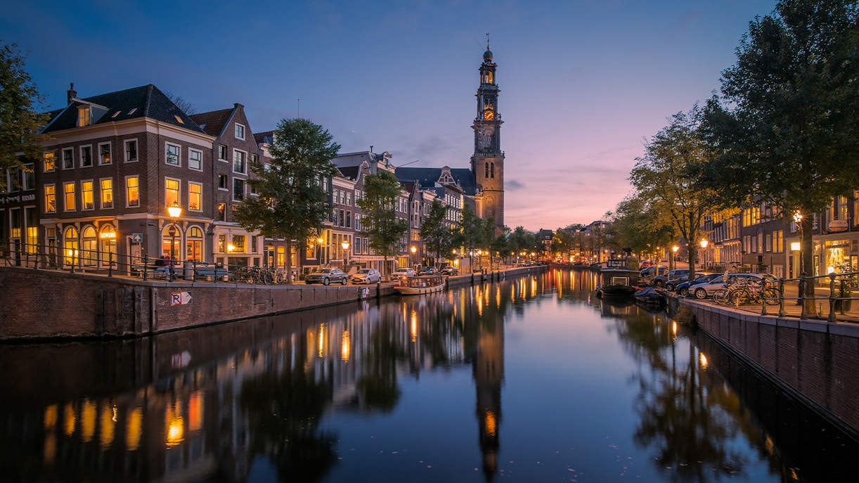 Canal view towards Anne Frank House and Westertoren church tower in Amsterdam at dusk.