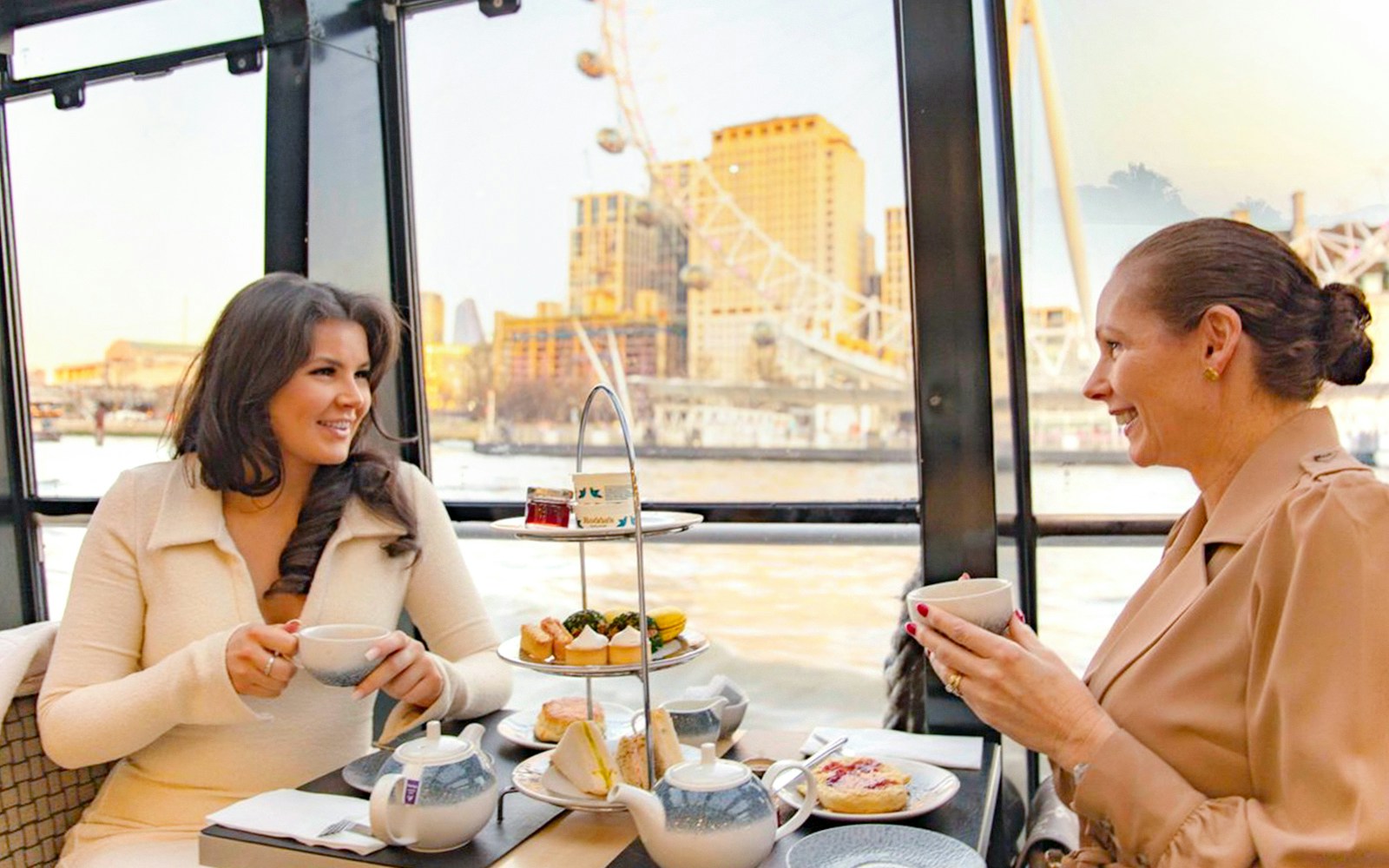 Guests on Thames River cruise enjoying tea and scones with London skyline in background