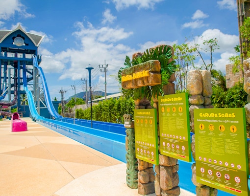 Water slide at Dragon's Drop, Andamanda Phuket with safety signs and lush surroundings.