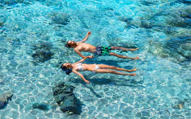 Couple floating in clear waters of La Maddalena Archipelago during motorboat tour.