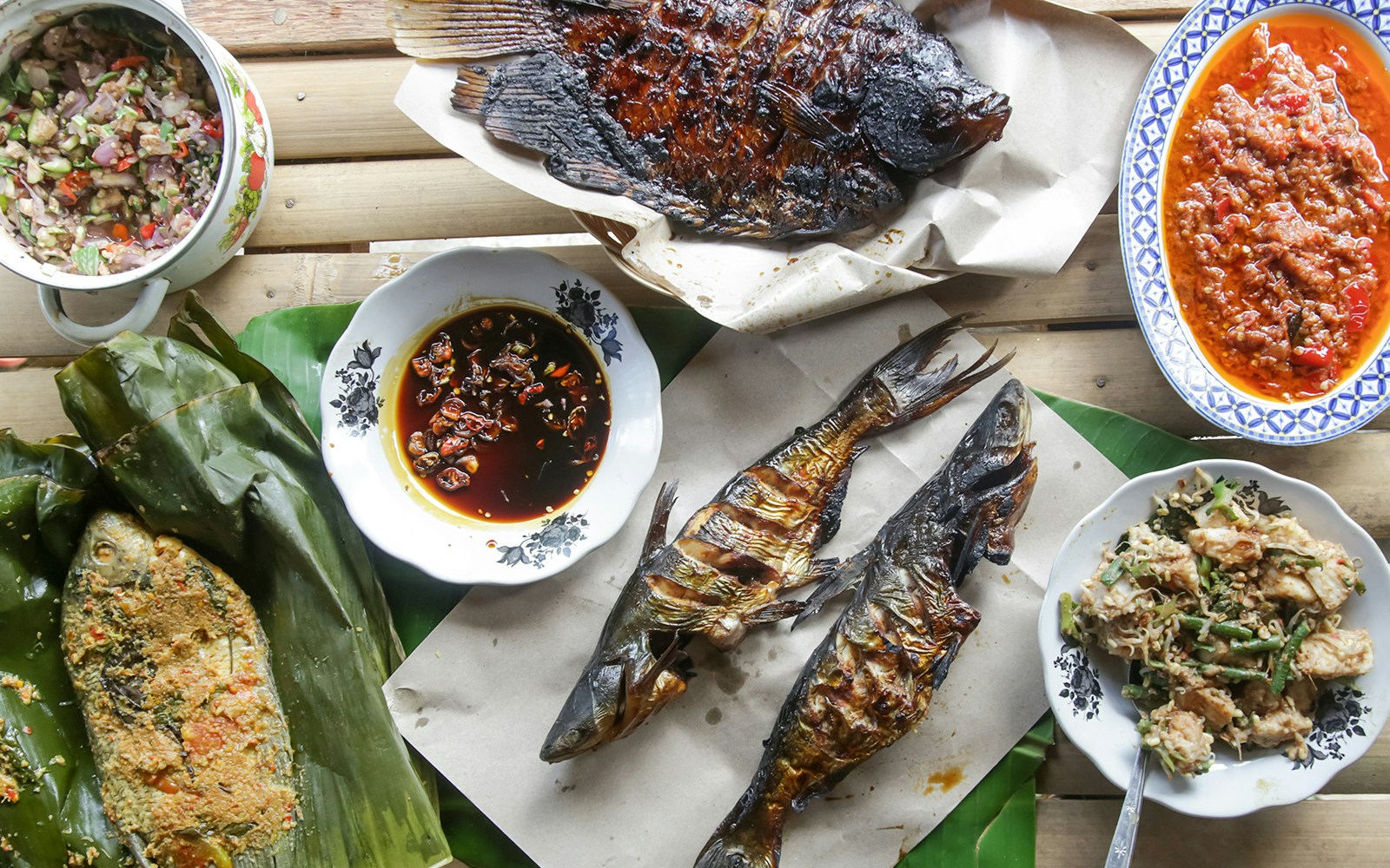 Grilled fish and sambal dishes in traditional Indonesian seafood spread.