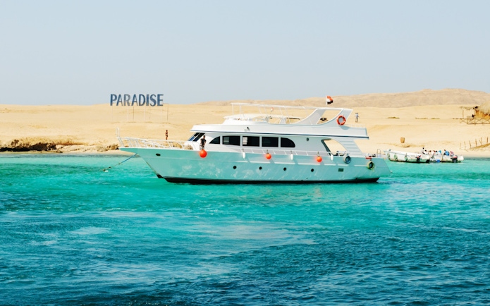 Cruise boat near Giftun Island, Hurghada with "Paradise" sign on sandy shore.