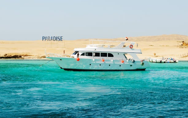 Cruise boat near Giftun Island, Hurghada with "Paradise" sign on sandy shore.