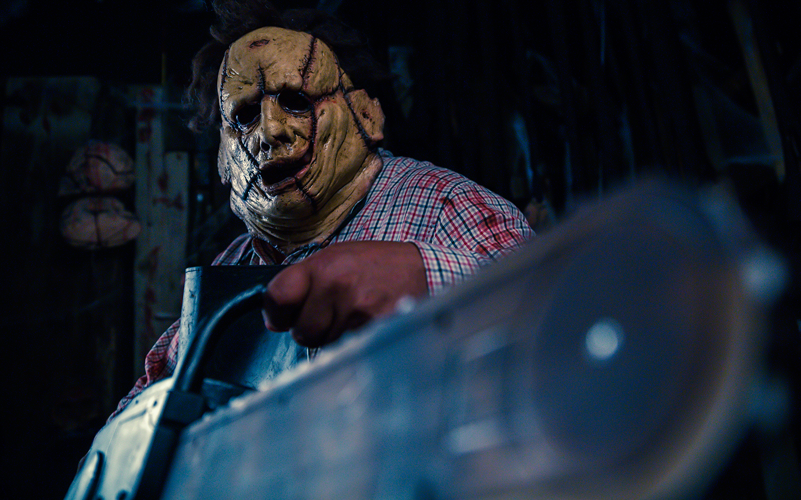 Person in a stitched mask holding a chainsaw inside a dimly lit haunted house.