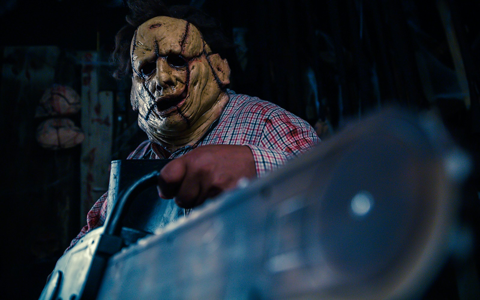 Person in a stitched mask holding a chainsaw inside a dimly lit haunted house.