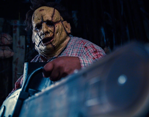 Person in a stitched mask holding a chainsaw inside a dimly lit haunted house.