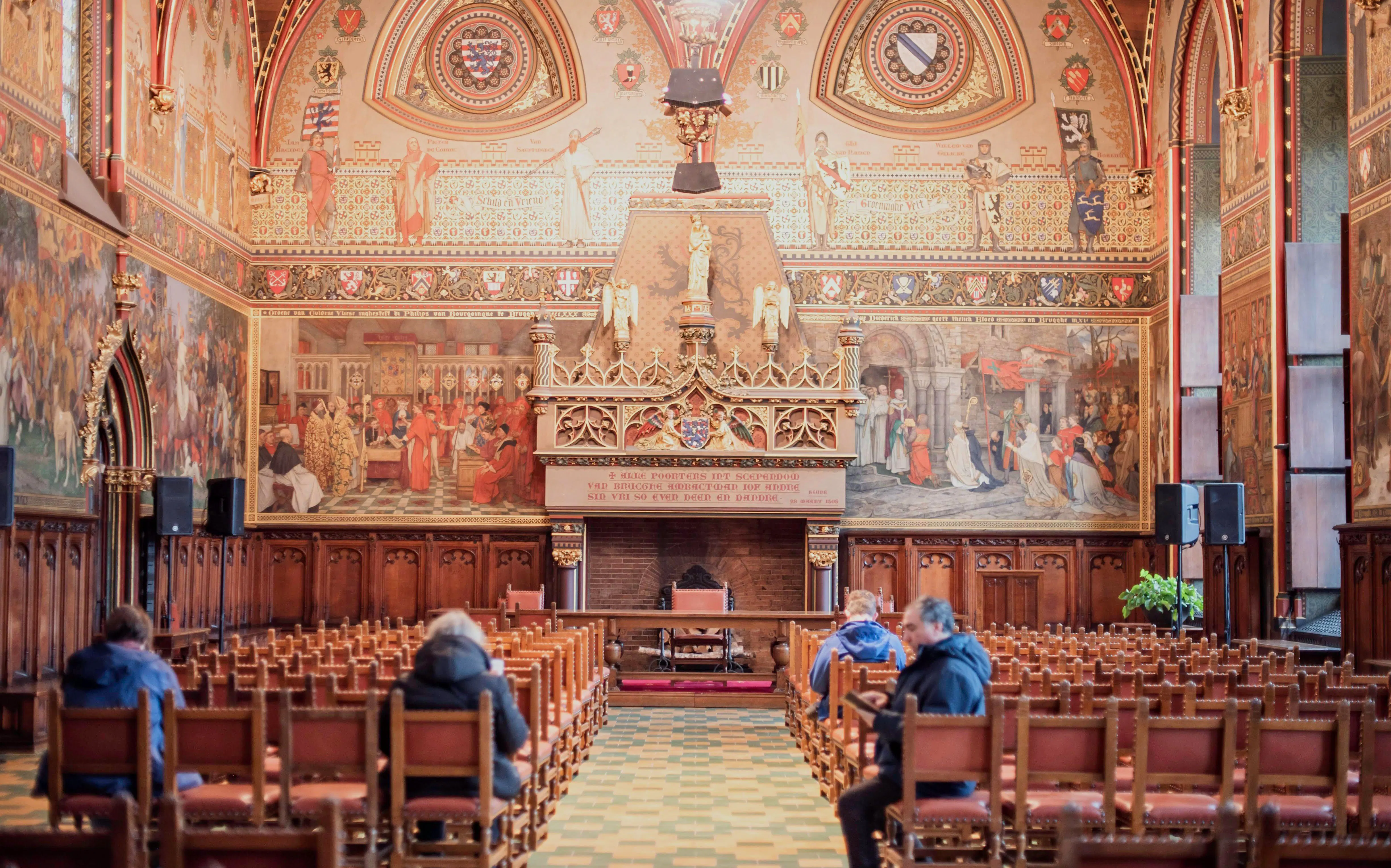 Bruges City Hall interior with ornate murals and wooden seating.