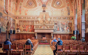 Bruges City Hall interior with ornate murals and wooden seating.