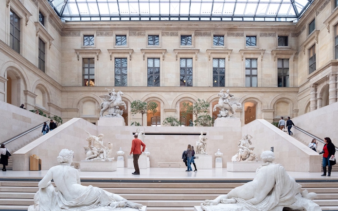 Tourists exploring the Louvre Museum's sculpture gallery in Paris, France.