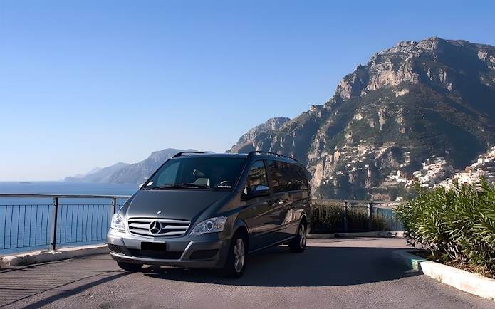 Minivan parked with Amalfi Coast cliffs and sea in the background.