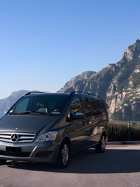 Minivan parked with Amalfi Coast cliffs and sea in the background.