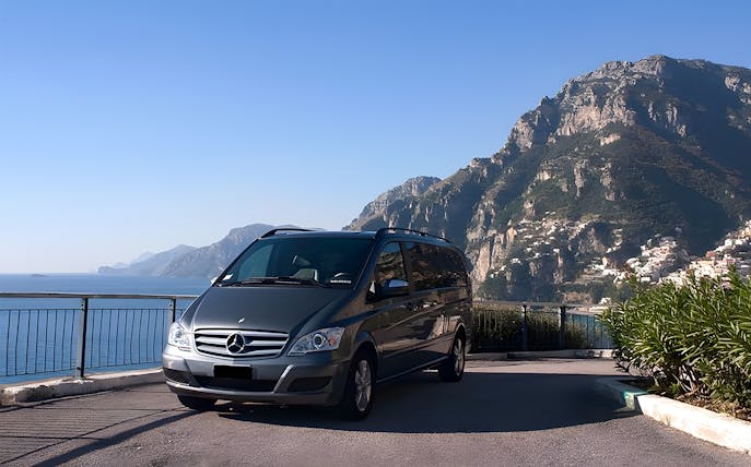 Minivan parked with Amalfi Coast cliffs and sea in the background.
