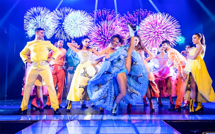 Dancers performing French Cancan at Paradis Latin in Cancun with fireworks in the background.