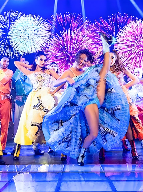 Dancers performing French Cancan at Paradis Latin in Cancun with fireworks in the background.