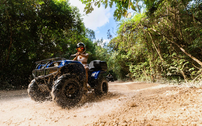 ATV rider navigating a muddy trail in Cancun's jungle adventure park.