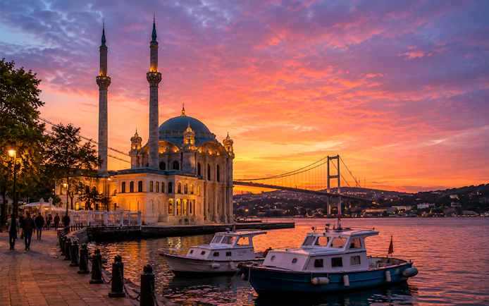 Galata Tower and Bosphorus Bridge at sunset with boats on the water.