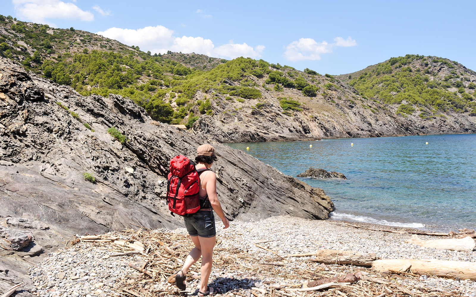 Hiker with red backpack on rocky Montjuïc trail by the sea.