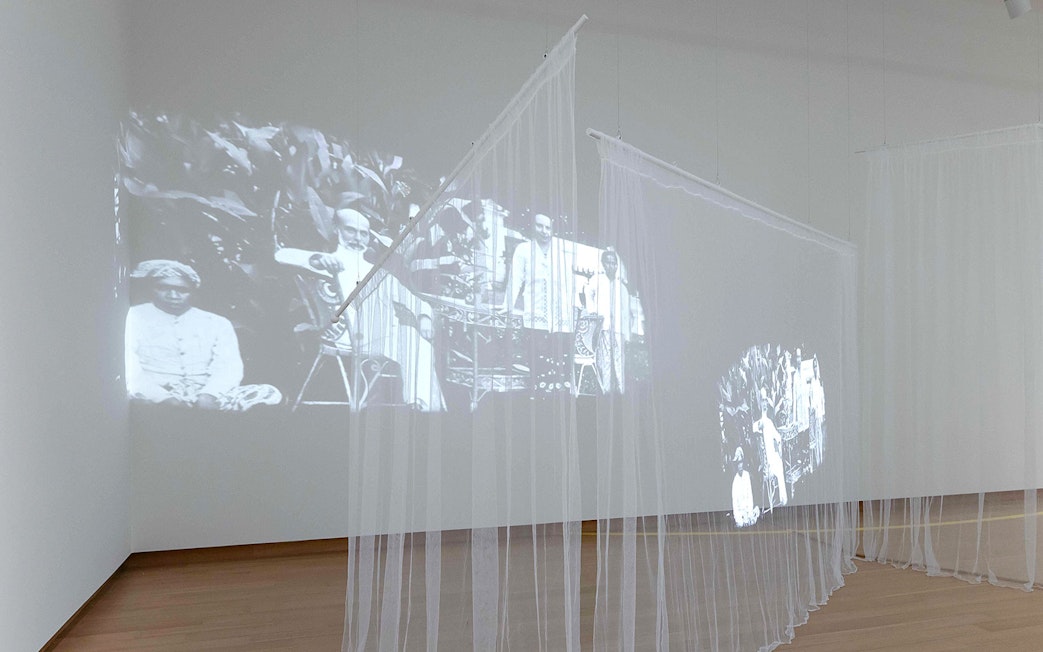Projection of colonial-era figures on sheer curtains at Stedelijk Museum exhibit.