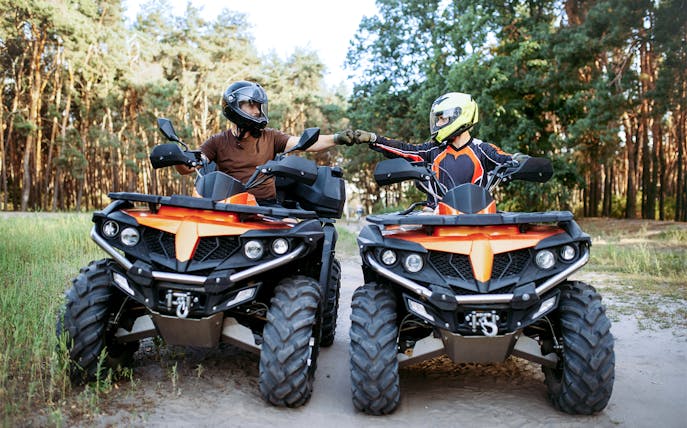 Two people on quad bikes in a forest near Zakopane, Poland, fist-bumping.