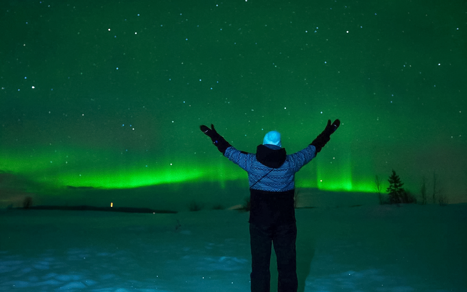 Person admiring Northern Lights over snowy Tromso landscape.