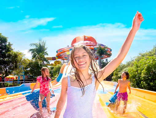 Children enjoying water slides at WhiteWater World, holding blue mats under a sunny sky.