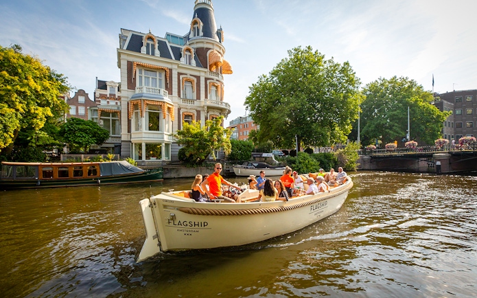 Luxury boat cruising Amsterdam canal near historic building.