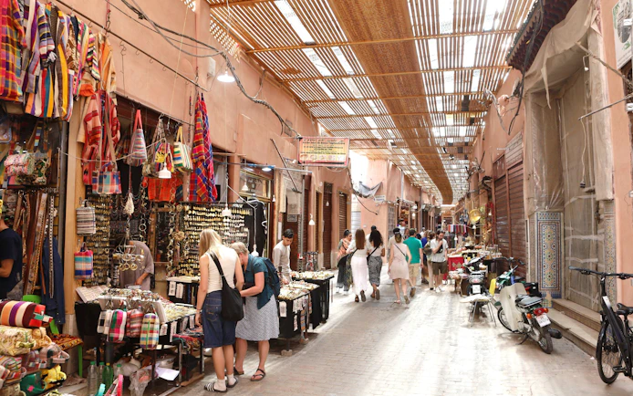 Marrakech Medina market with tourists browsing colorful textiles and crafts.