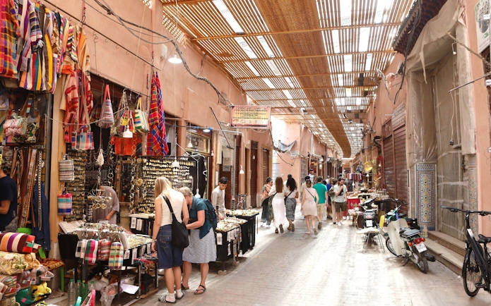 Marrakech Medina market with tourists browsing colorful textiles and crafts.