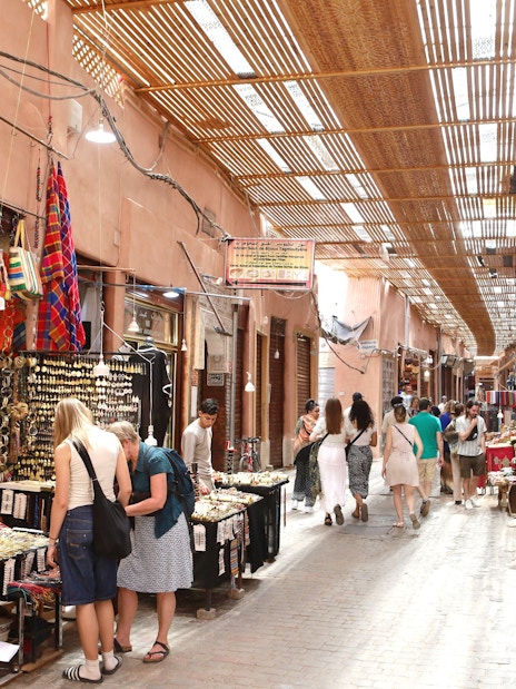Marrakech Medina market with tourists browsing colorful textiles and crafts.