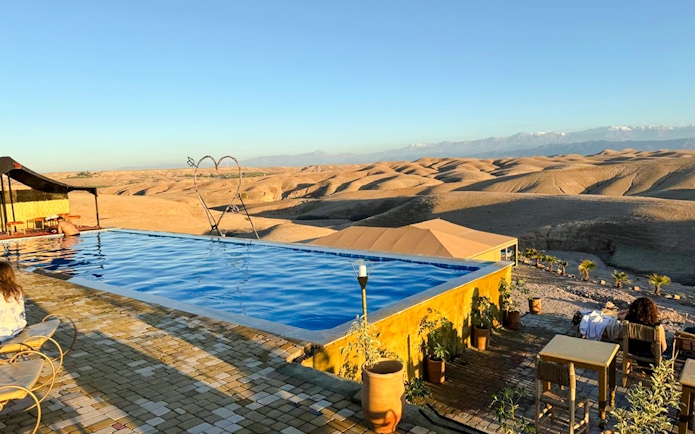 Infinity pool overlooking Agafay Desert near Marrakesh with distant mountains.